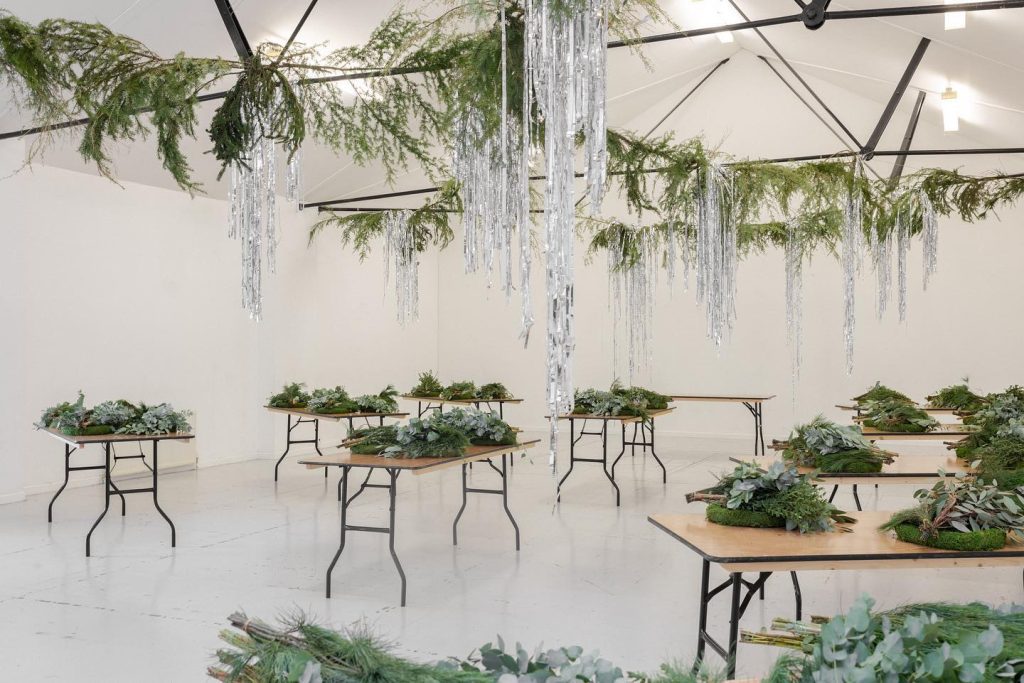 Large Hall with White Walls. and Grey Floor showing tables laden with Green Foliage